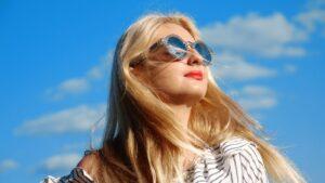 "Enjoy a Bright and Healthy Summer with Essential Eye Care Tips. Blonde haired lady wearing sunglasses in front of a blue sky
