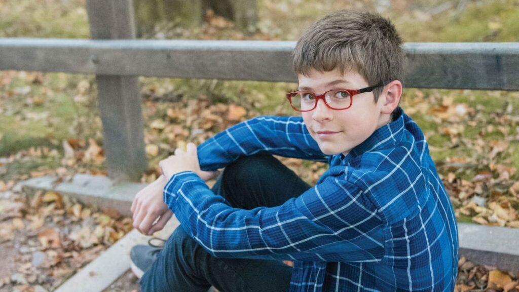 Boy in his early teens sitting on the ground outside, wearing glasses. EK Eyewear Belfast.