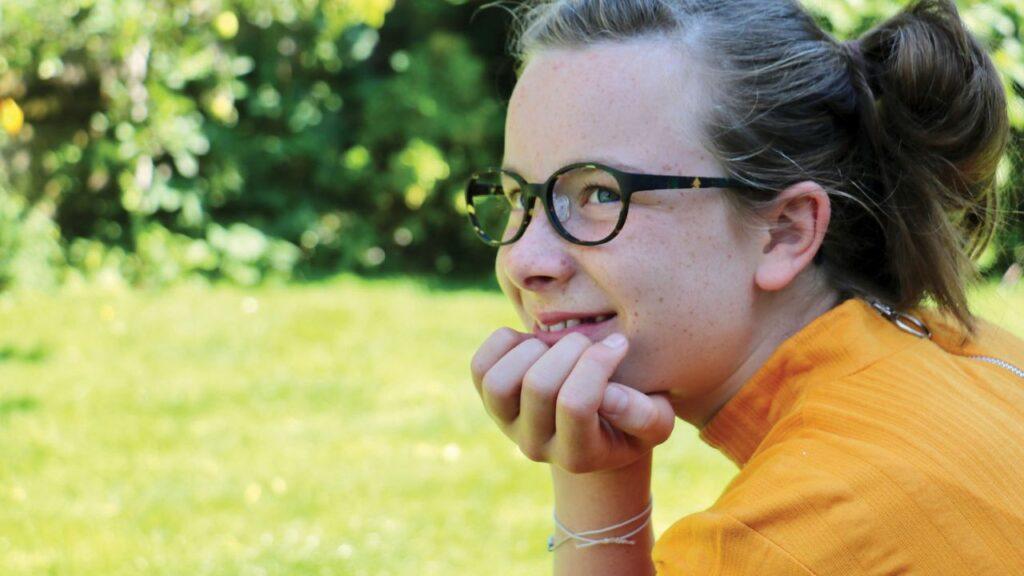 Girl with glasses on sitting in a park or garden. EK Eyewear Belfast.